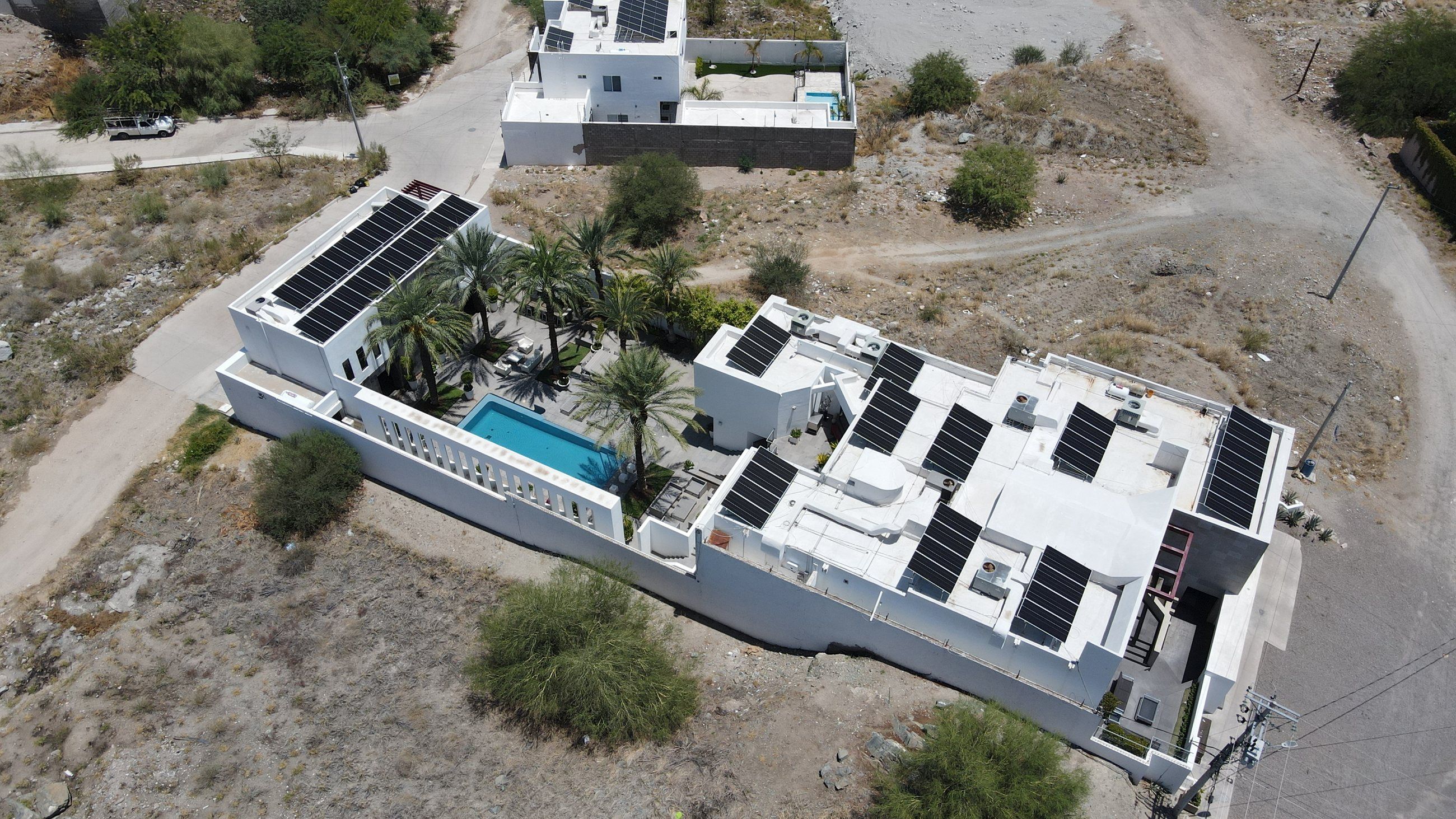 Casa de dos pisos en Hermosillo con alberca y palmeras, con filas de paneles solares en las azoteas, vista desde dron