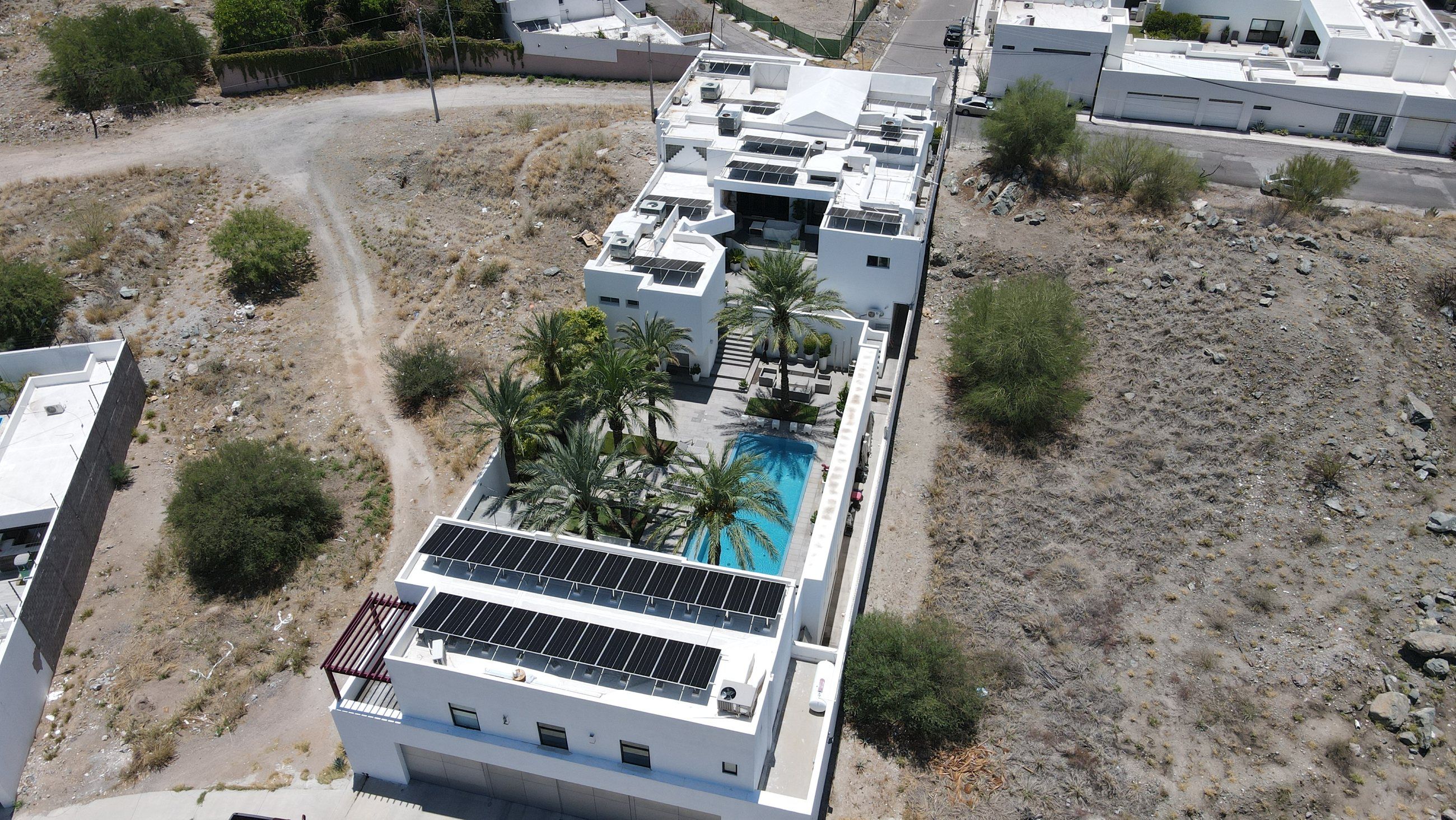 Casa de dos pisos con alberca y palmeras, con filas de paneles solares en las azoteas, vista desde dron
