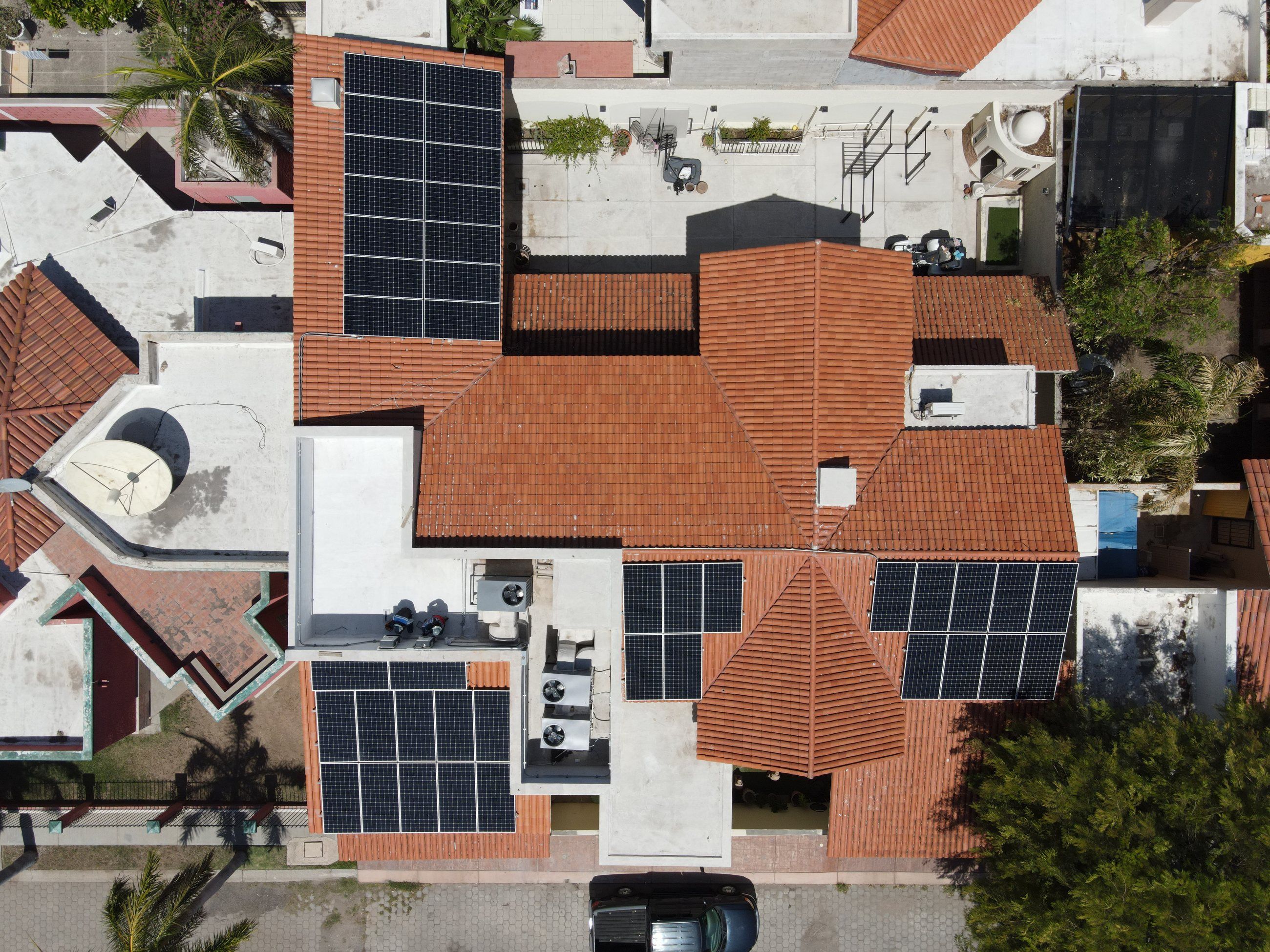 Casa con techos de teja roja y paneles solares en varias secciones de la azotea, vista desde arriba con dron