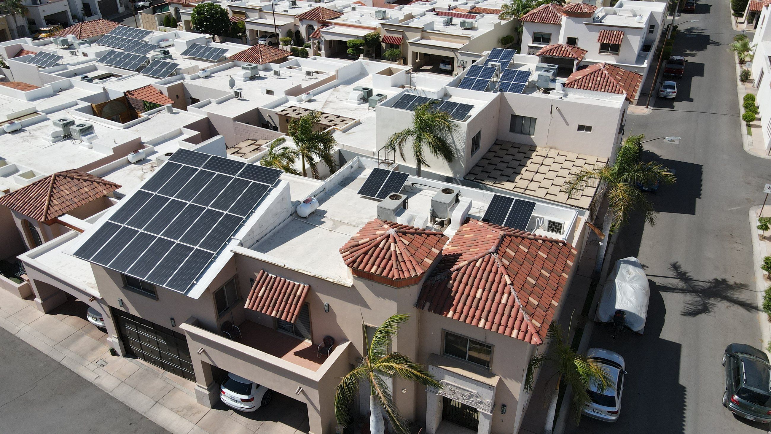 Casa de dos pisos con techos de teja y paneles solares en la azotea, en un fraccionamiento con varias casas solares, vista desde dron