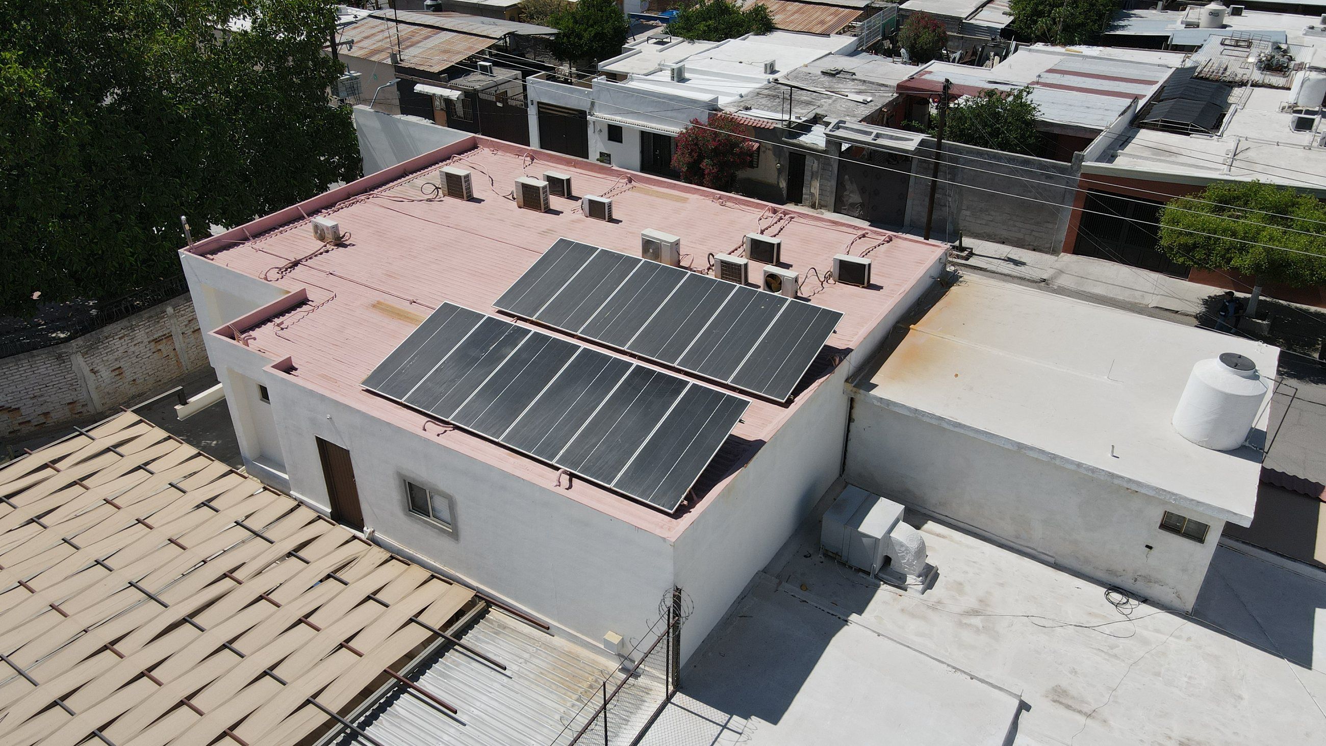 Local comercial en Hermosillo con dos filas de paneles solares sobre la azotea, entre casas de la colonia, visto desde dron