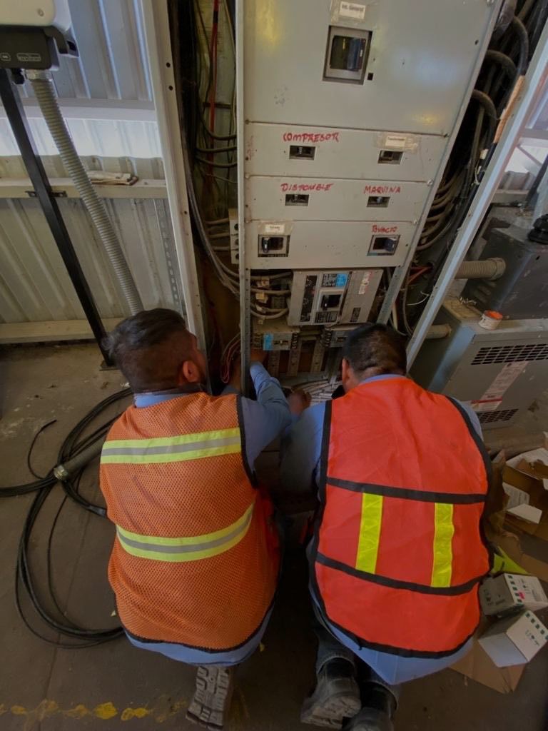 Dos electricistas con chaleco reflejante haciendo las conexiones de un tablero eléctrico
