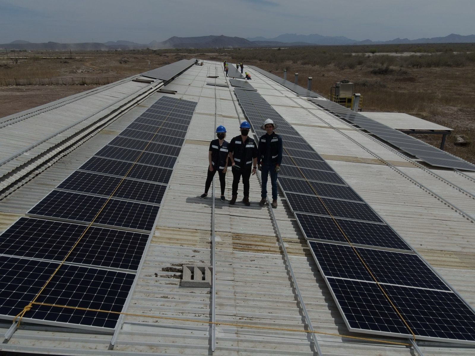 Tres personas de Solarix con casco y chaleco entre filas de paneles recién montados sobre una nave de lámina, con cerros al fondo