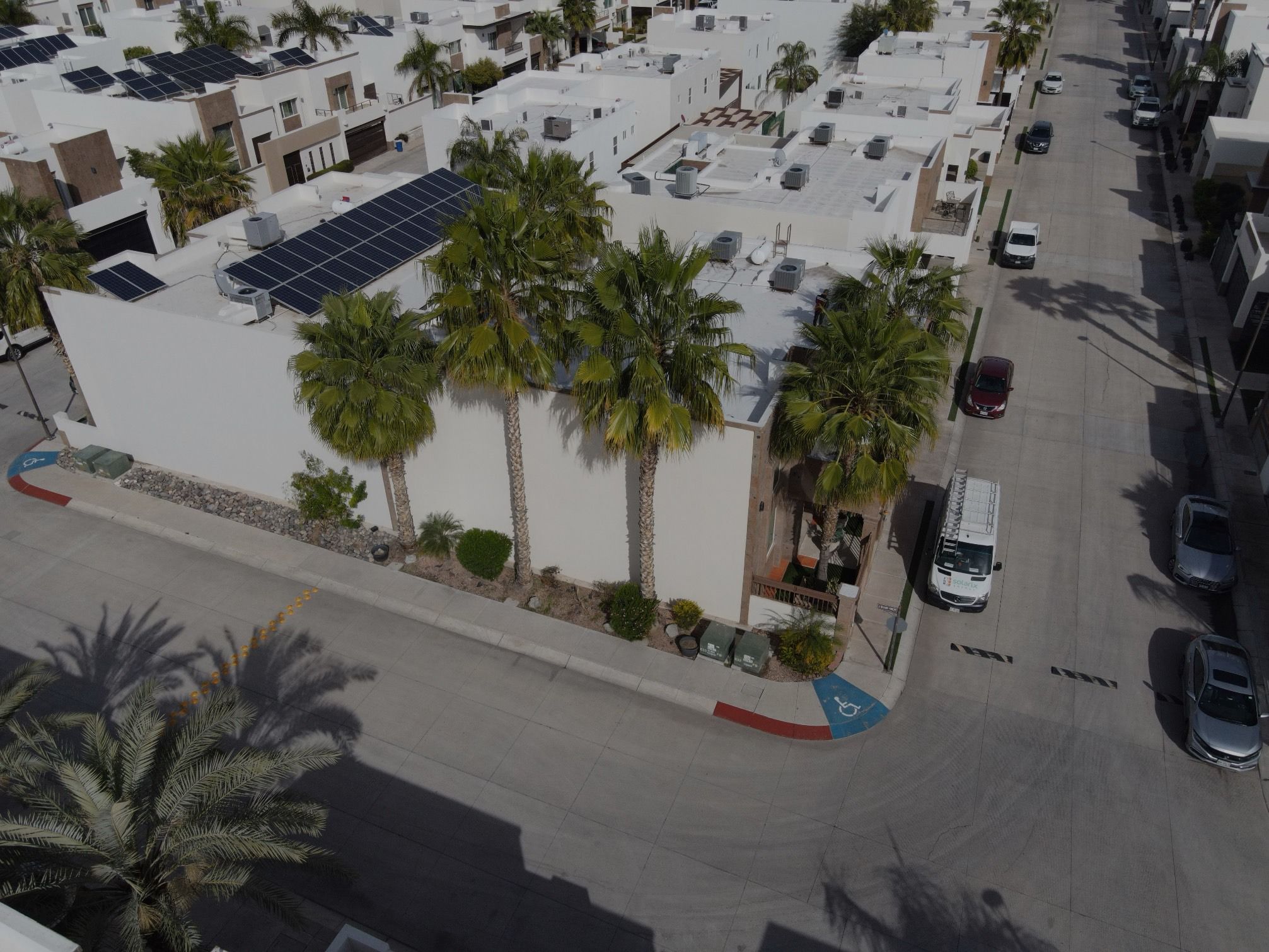 Casa de dos pisos con palmeras en una esquina de fraccionamiento, con paneles solares en la azotea, vista desde dron