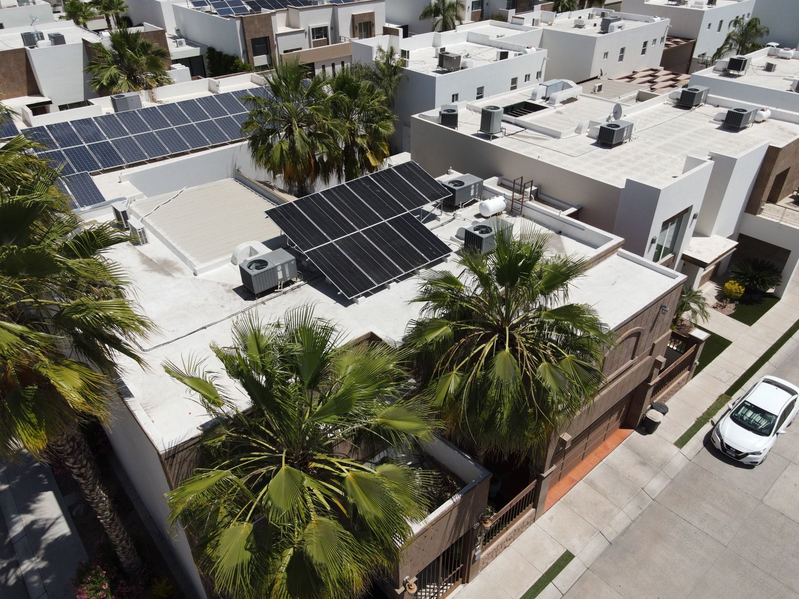 Azoteas de casas vistas desde dron, con arreglos de paneles solares junto a los equipos de minisplit, tinacos y palmeras