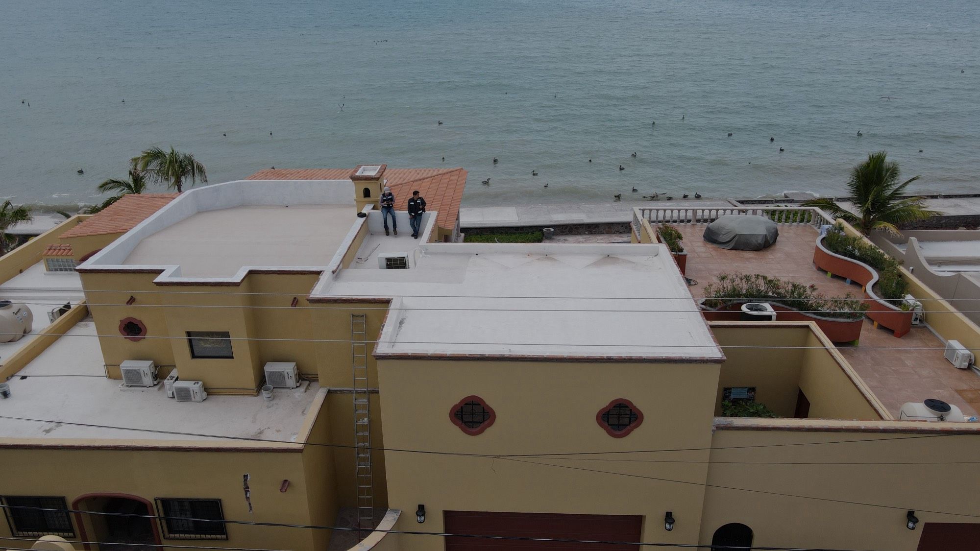 Dos técnicos de Solarix sobre la azotea de una casa frente al mar, vistos desde el dron durante una visita técnica